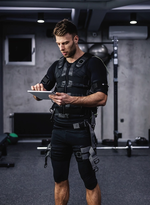 Man wearing EMS training gear while using a tablet in a gym